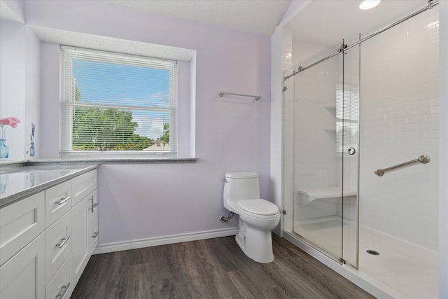 bathroom featuring wood finished floors, a stall shower, toilet, vanity, and baseboards