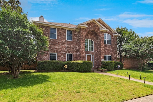 traditional-style house with a chimney, a front yard, and brick siding