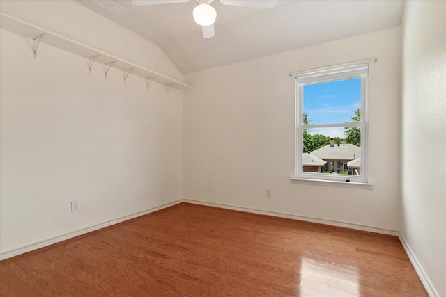 empty room with wood finished floors, a ceiling fan, lofted ceiling, and baseboards