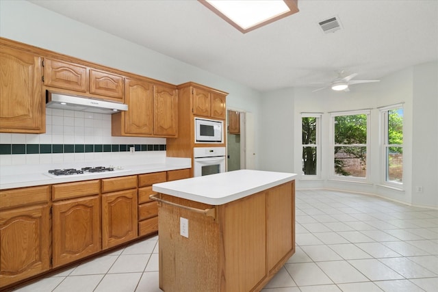 kitchen featuring under cabinet range hood, white appliances, light countertops, and light tile patterned floors