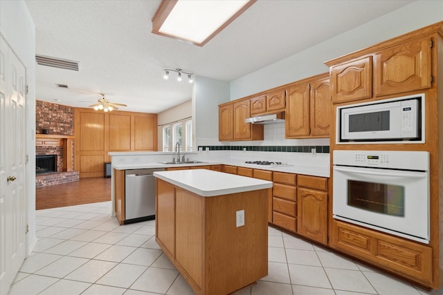 kitchen with white appliances, a sink, light tile patterned floors, light countertops, and a center island
