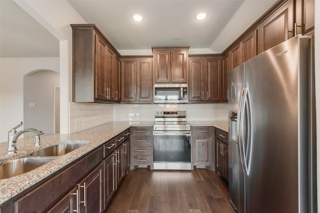 4505 Ridgehurst Ln, Fort Worth, TX 76036 - kitchen featuring appliances with stainless steel finishes, a sink, arched walkways, dark wood-type flooring, and light stone counters
