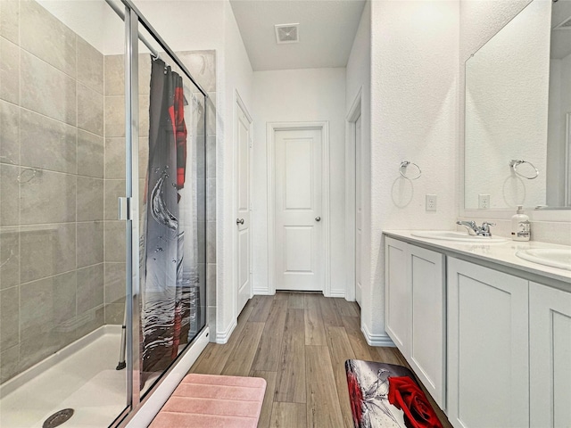 8309 Caracara Dr, Mckinney, TX 75071 - bathroom featuring a stall shower, wood finished floors, double vanity, a textured wall, and baseboards