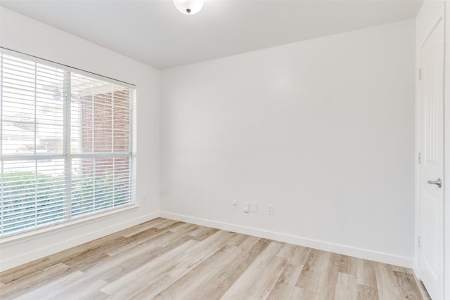 spare room featuring light wood finished floors, healthy amount of natural light, and baseboards