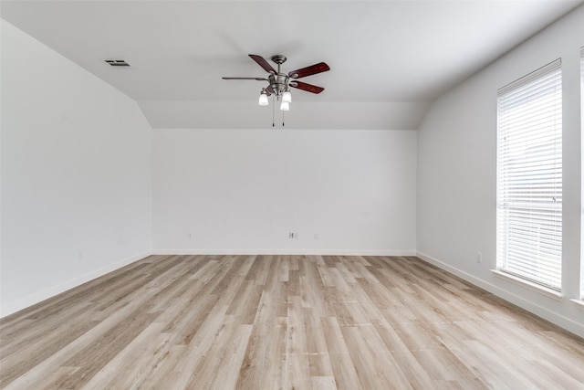 spare room featuring vaulted ceiling, light wood-style flooring, ceiling fan, plenty of natural light, and baseboards