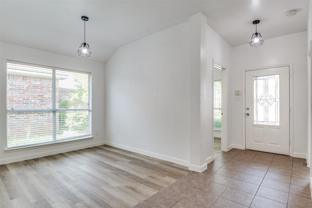 foyer featuring plenty of natural light, baseboards, vaulted ceiling, and light tile patterned floors