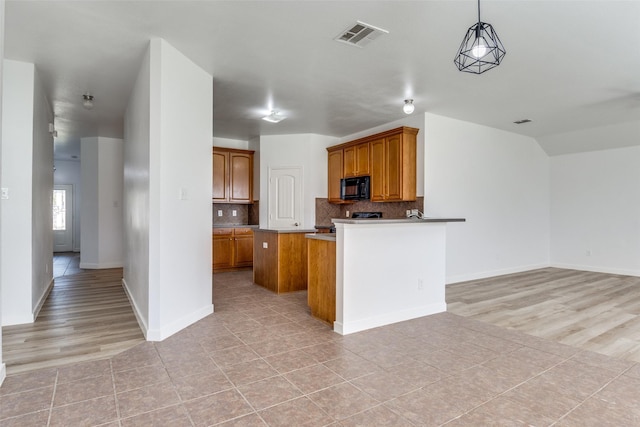 kitchen featuring black microwave, brown cabinetry, backsplash, open floor plan, and hanging light fixtures