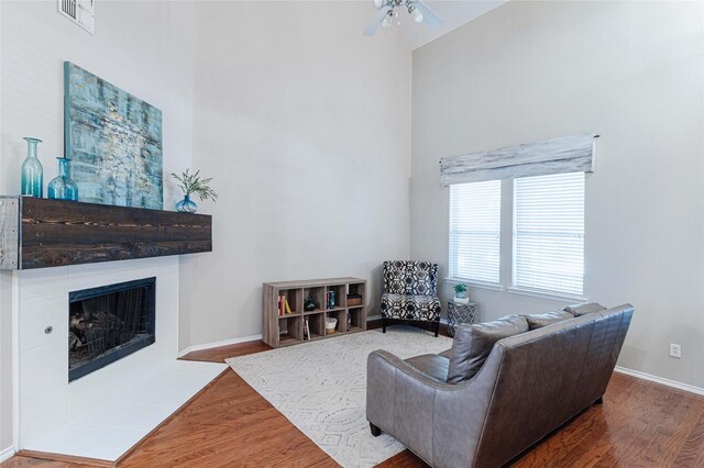 9908 Summer Sweet Dr, Mckinney, TX 75072 - living area featuring ceiling fan, wood finished floors, a tiled fireplace, a high ceiling, and baseboards