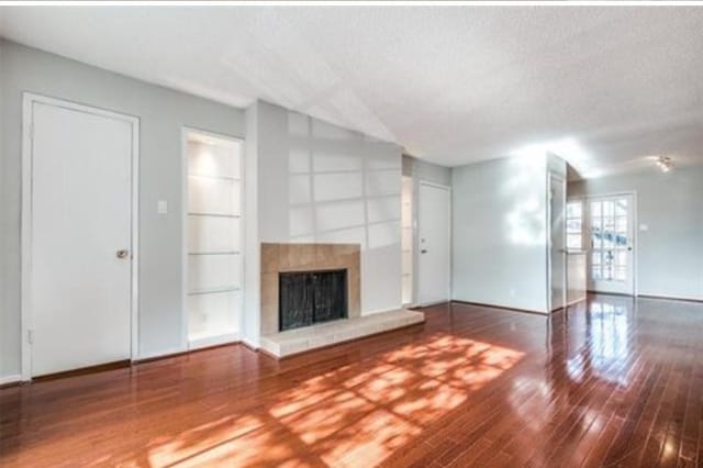 5232 Fleetwood Oaks Ave Unit 216, Dallas, TX 75235 - unfurnished living room featuring baseboards, built in shelves, a fireplace with raised hearth, wood-type flooring, and a textured ceiling