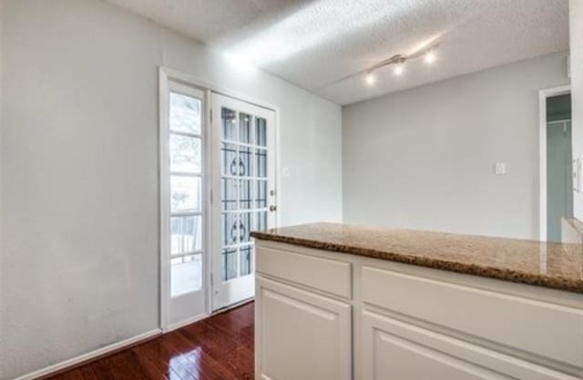 5232 Fleetwood Oaks Ave Unit 216, Dallas, TX 75235 - kitchen with dark wood-style floors, stone counters, white cabinets, a textured ceiling, and rail lighting