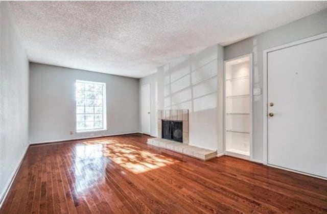 5232 Fleetwood Oaks Ave Unit 216, Dallas, TX 75235 - unfurnished living room featuring a textured ceiling, hardwood / wood-style floors, a tiled fireplace, and baseboards