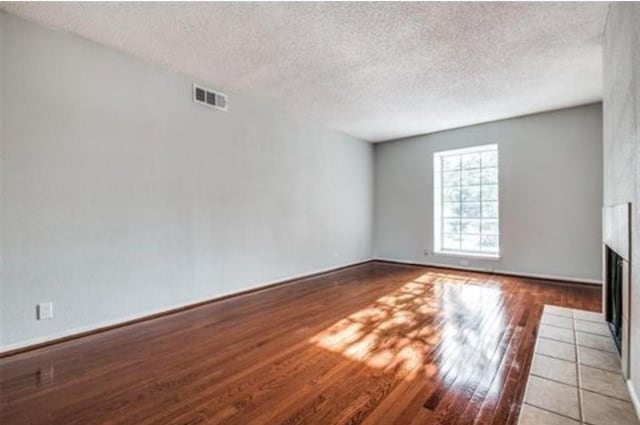 5232 Fleetwood Oaks Ave Unit 216, Dallas, TX 75235 - unfurnished living room featuring a tile fireplace, light wood-style flooring, a textured ceiling, and baseboards