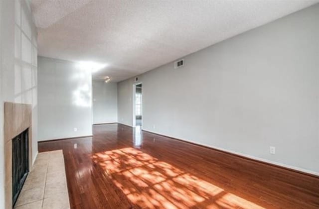 5232 Fleetwood Oaks Ave Unit 216, Dallas, TX 75235 - unfurnished living room featuring a fireplace with raised hearth, light wood-style floors, a textured ceiling, and baseboards