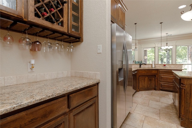 196 Ellis Creek Dr, Weatherford, TX 76085 - kitchen featuring stainless steel fridge, brown cabinetry, pendant lighting, light stone countertops, and glass insert cabinets