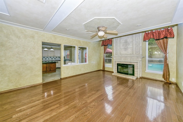 unfurnished living room with wood finished floors, ceiling fan, a fireplace, baseboards, and ornamental molding