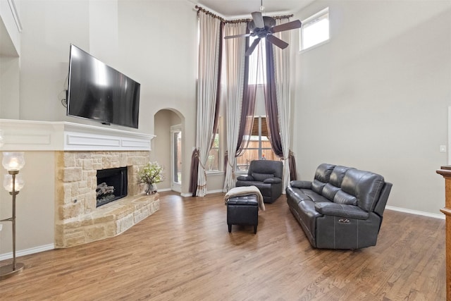2671 Marshall Dr, Frisco, TX 75033 - living area featuring a stone fireplace, arched walkways, a towering ceiling, a ceiling fan, and wood finished floors