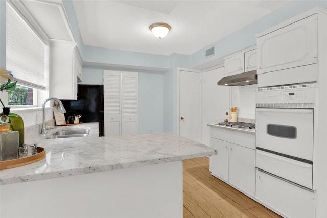 kitchen with white oven, a sink, a warming drawer, under cabinet range hood, and white cabinetry