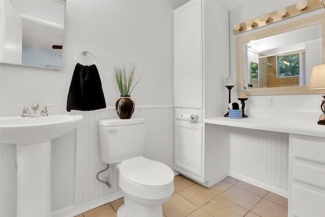 bathroom featuring toilet, tile patterned flooring, a sink, a shower, and wainscoting
