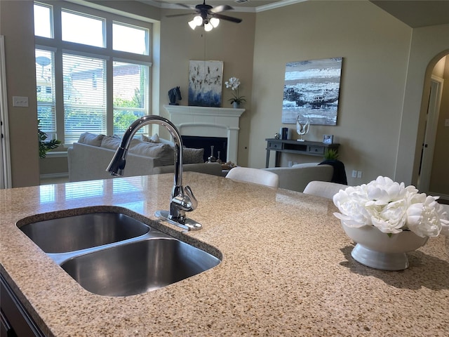 8740 Running River Ln, Fort Worth, TX 76131 - kitchen featuring a sink, arched walkways, a ceiling fan, light stone countertops, and a fireplace