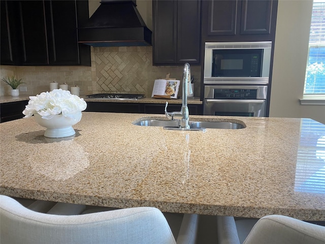 8740 Running River Ln, Fort Worth, TX 76131 - kitchen featuring premium range hood, stainless steel gas cooktop, a sink, decorative backsplash, and dark cabinetry