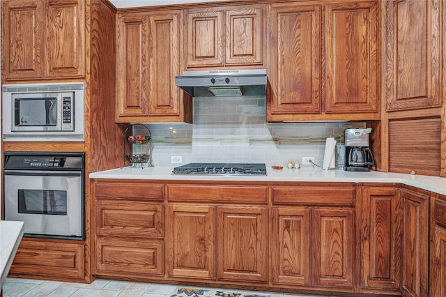 11086 Tenison Ln, Frisco, TX 75033 - kitchen with stainless steel appliances, under cabinet range hood, brown cabinets, and backsplash