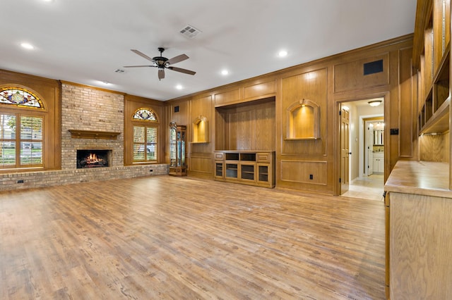 3740 Chimney Ridge Dr, Waco, TX 76708 - unfurnished living room featuring ceiling fan, light wood-style floors, wooden walls, a brick fireplace, and crown molding