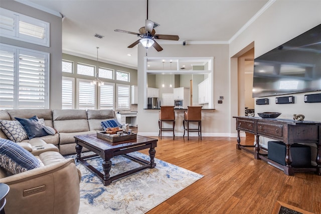 living area featuring a ceiling fan, light wood-style flooring, crown molding, baseboards, and a chandelier
