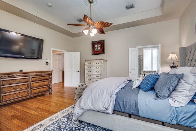 bedroom featuring wood finished floors, a raised ceiling, and a ceiling fan