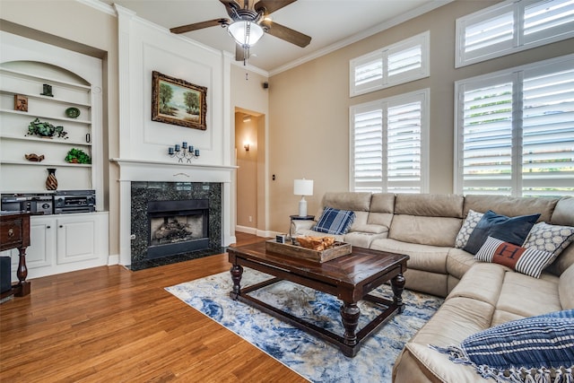 living area with ornamental molding, a ceiling fan, wood finished floors, a high end fireplace, and built in features