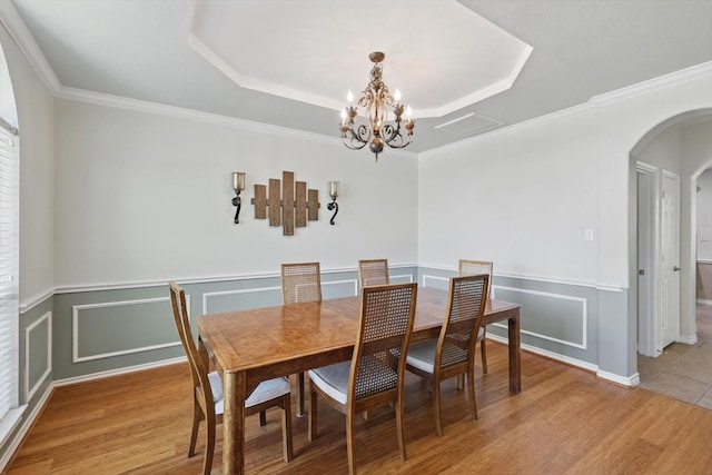 1601 Manchester Way, Corinth, TX 76210 - dining space featuring arched walkways, a chandelier, light wood finished floors, a wainscoted wall, and a tray ceiling