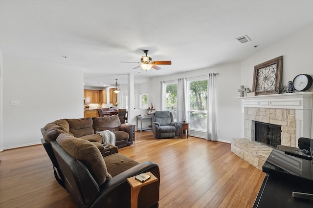 1601 Manchester Way, Corinth, TX 76210 - living room featuring a ceiling fan, light wood-style flooring, a stone fireplace, and baseboards