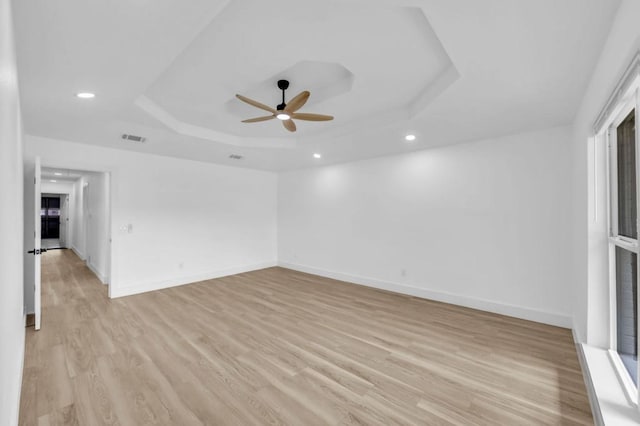 spare room with a raised ceiling, a ceiling fan, light wood-type flooring, baseboards, and recessed lighting