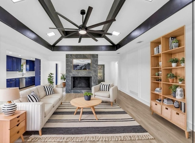 living area featuring light wood-type flooring, ceiling fan, a premium fireplace, beamed ceiling, and high vaulted ceiling