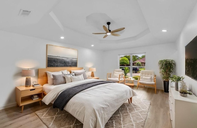 bedroom with a raised ceiling, light wood-type flooring, recessed lighting, ceiling fan, and baseboards