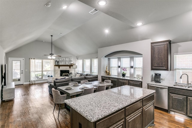 936 Mangrove Dr, Fate, TX 75087 - kitchen with stainless steel dishwasher, a fireplace, dark brown cabinets, wood finished floors, and light stone counters