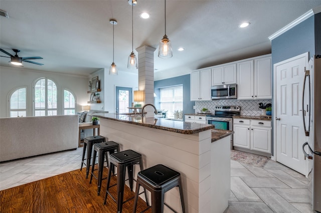 8209 Clear Bay Dr, Mckinney, TX 75072 - kitchen featuring appliances with stainless steel finishes, open floor plan, ceiling fan, white cabinets, and a breakfast bar area