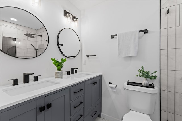 full bath with toilet, a tile shower, double vanity, and baseboards