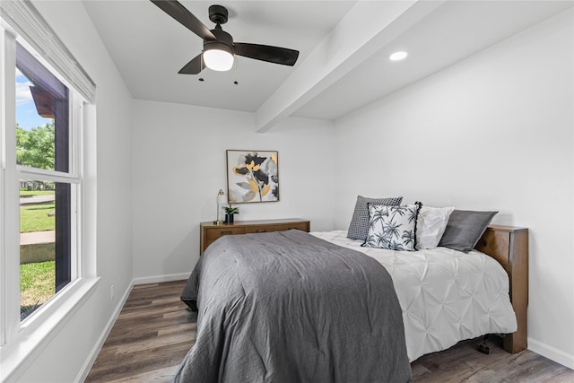 bedroom with multiple windows, wood finished floors, baseboards, ceiling fan, and beamed ceiling