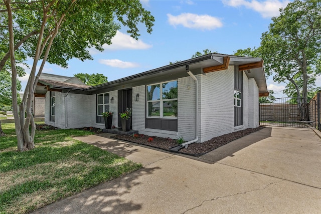 view of front facade featuring brick siding, a front lawn, a gate, and concrete driveway