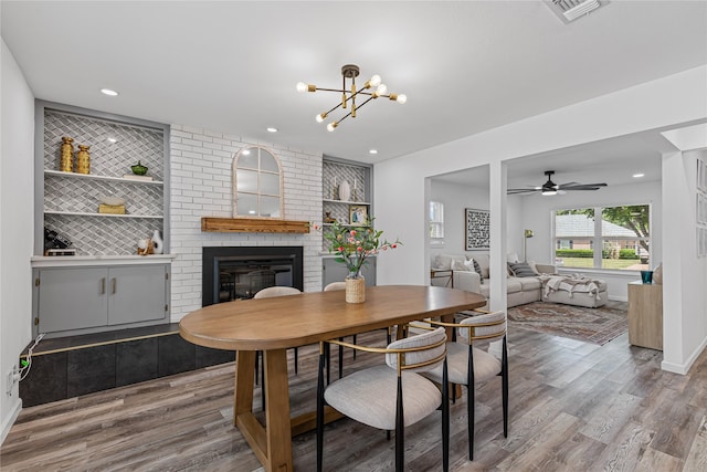 dining room featuring wood finished floors, a brick fireplace, recessed lighting, baseboards, and a chandelier