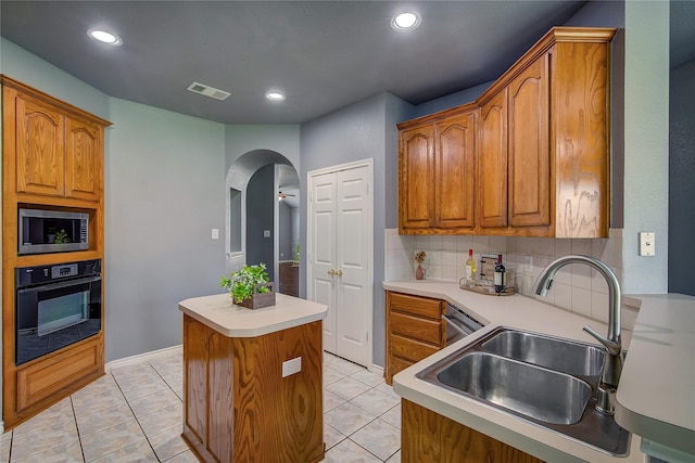 kitchen featuring black oven, stainless steel microwave, a sink, arched walkways, and a center island
