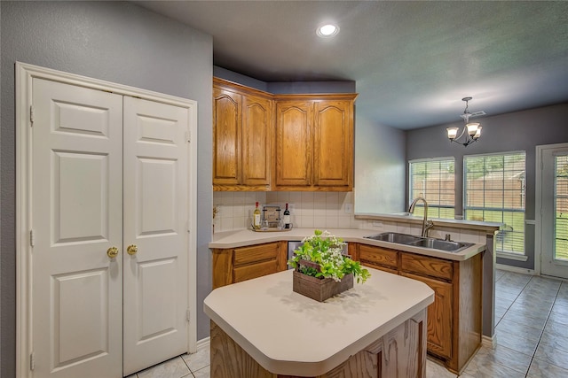 kitchen with a sink, a peninsula, brown cabinets, light countertops, and light tile patterned floors