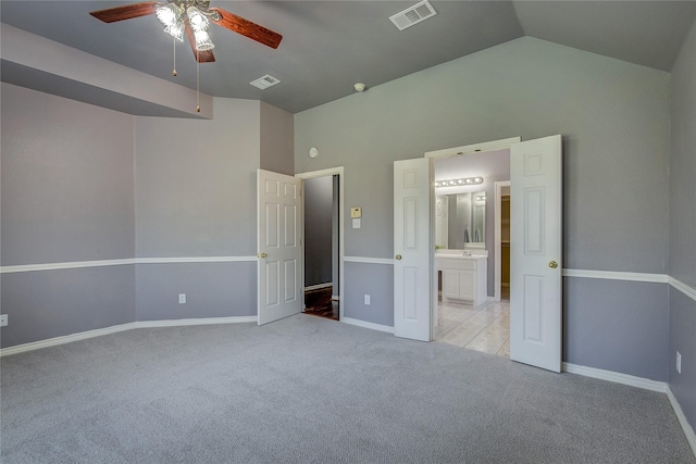 unfurnished bedroom featuring light carpet, vaulted ceiling, baseboards, ensuite bathroom, and ceiling fan