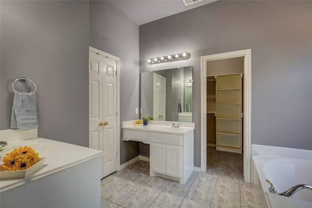 full bathroom featuring vanity, a bath, tile patterned floors, a walk in closet, and baseboards