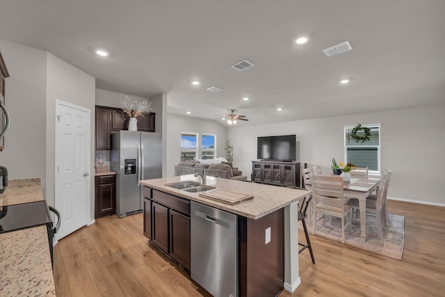 3005 Sherco Rd, Waco, TX 76655 - kitchen featuring stainless steel appliances, a sink, light wood-style flooring, dark brown cabinets, and a kitchen island with sink