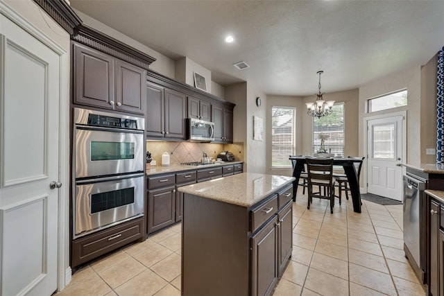 15606 Fox Meadow Ln, Frisco, TX 75035 - kitchen featuring appliances with stainless steel finishes, backsplash, a chandelier, light tile patterned floors, and light stone countertops