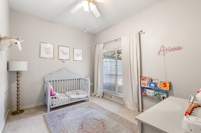 carpeted bedroom featuring a nursery area, baseboards, and a ceiling fan
