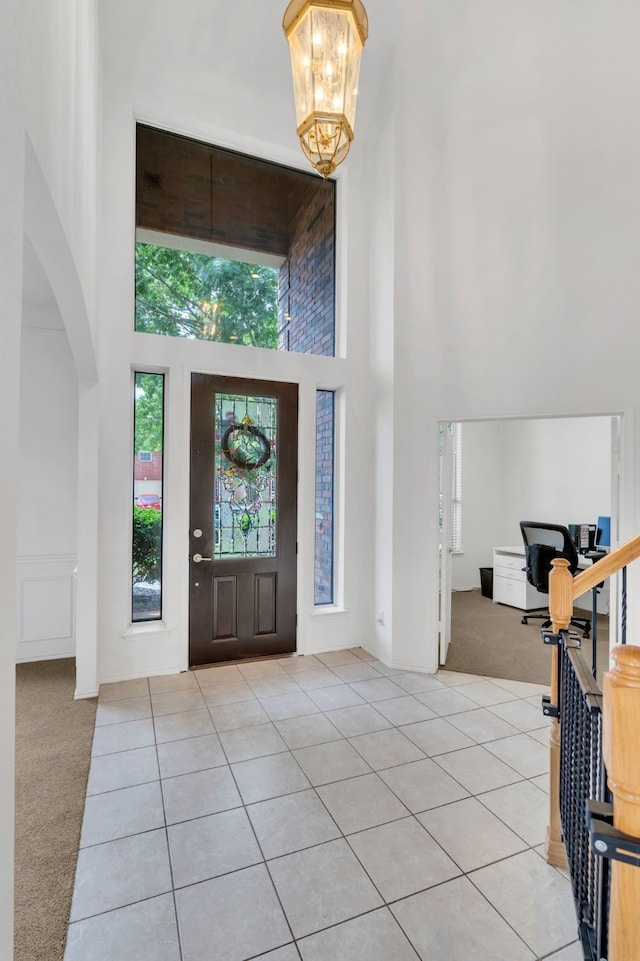 foyer with a high ceiling, arched walkways, light carpet, light tile patterned floors, and a chandelier