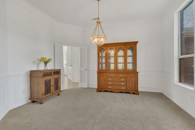 carpeted spare room featuring a chandelier, ornamental molding, wainscoting, and a decorative wall