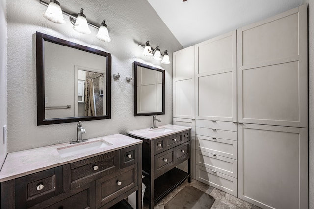 4242 N Capistrano Dr Unit 174, Dallas, TX 75287 - bathroom with vaulted ceiling, two vanities, and a textured wall